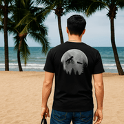A man wearing a black t-shirt with a large Spielberg tribute graphic on the back, walking on a beach promenade with palm trees in the background.
