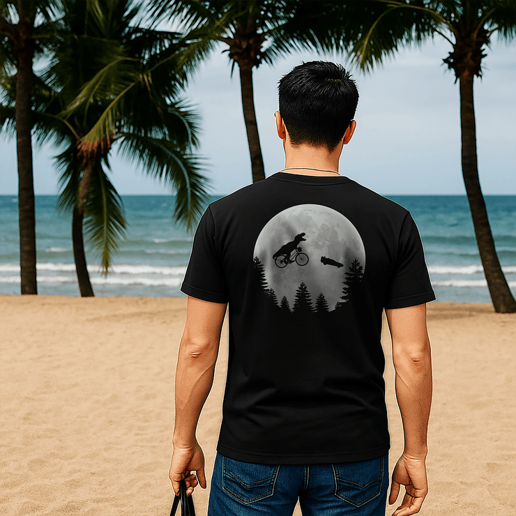 A man wearing a black t-shirt with a large Spielberg tribute graphic on the back, walking on a beach promenade with palm trees in the background.